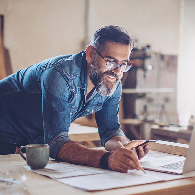 Smiling, casual man with beard, working with pencil, paper and laptop