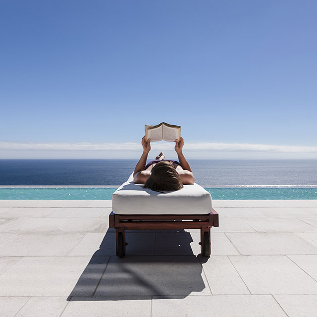 Lady reading book next to pool overlooking the beach.