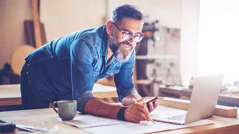 A smiling, bearded man reviews some information on his laptop’s screen. 